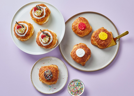 A variety of Schulstad Almond Danish Doughnuts decorated with colorful icings or filled with whipped cream