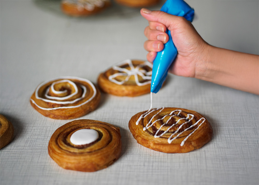 Baker Decorating Cinnamon Swirl Danish Pastries with white icing included in case